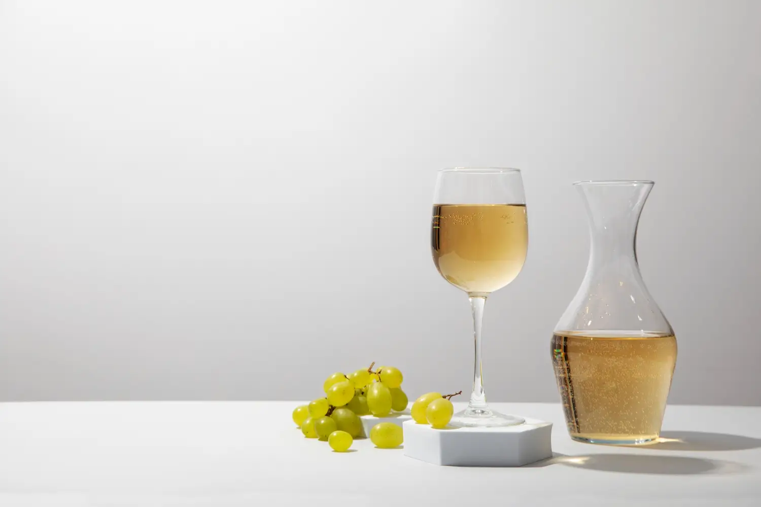 Verre de vin blanc posé à côté de raisins sur une surface blanche