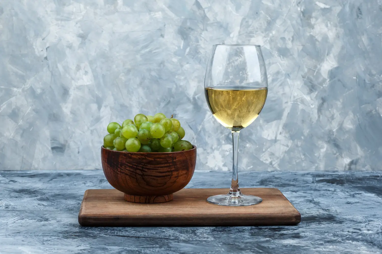 Verre de vin blanc et bol de raisins verts sur fond gris